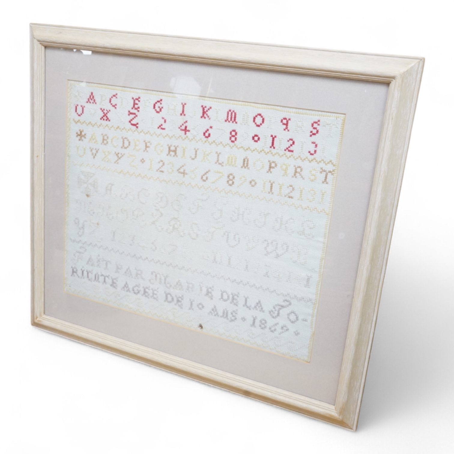 A large French 19th century cross stitch sampler. Dated 1867 by Marie De La Torcote aged 10 years. Worked in red and pastel threads.36cm wide x 44cm high. Condition - two rust stains to left side and a dark thread to bot
